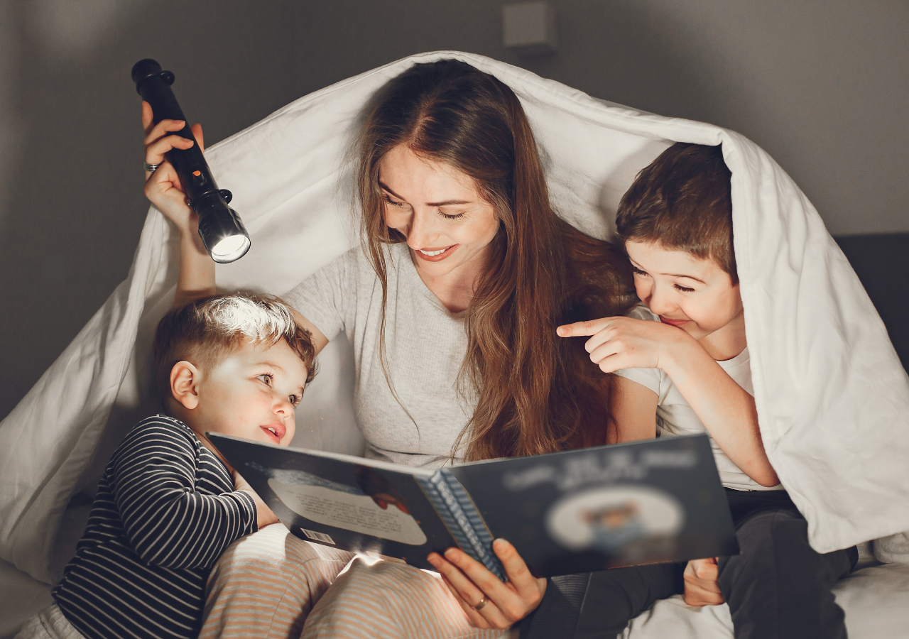 Mom and 2 boys reading a story under a blanket with a flashlight